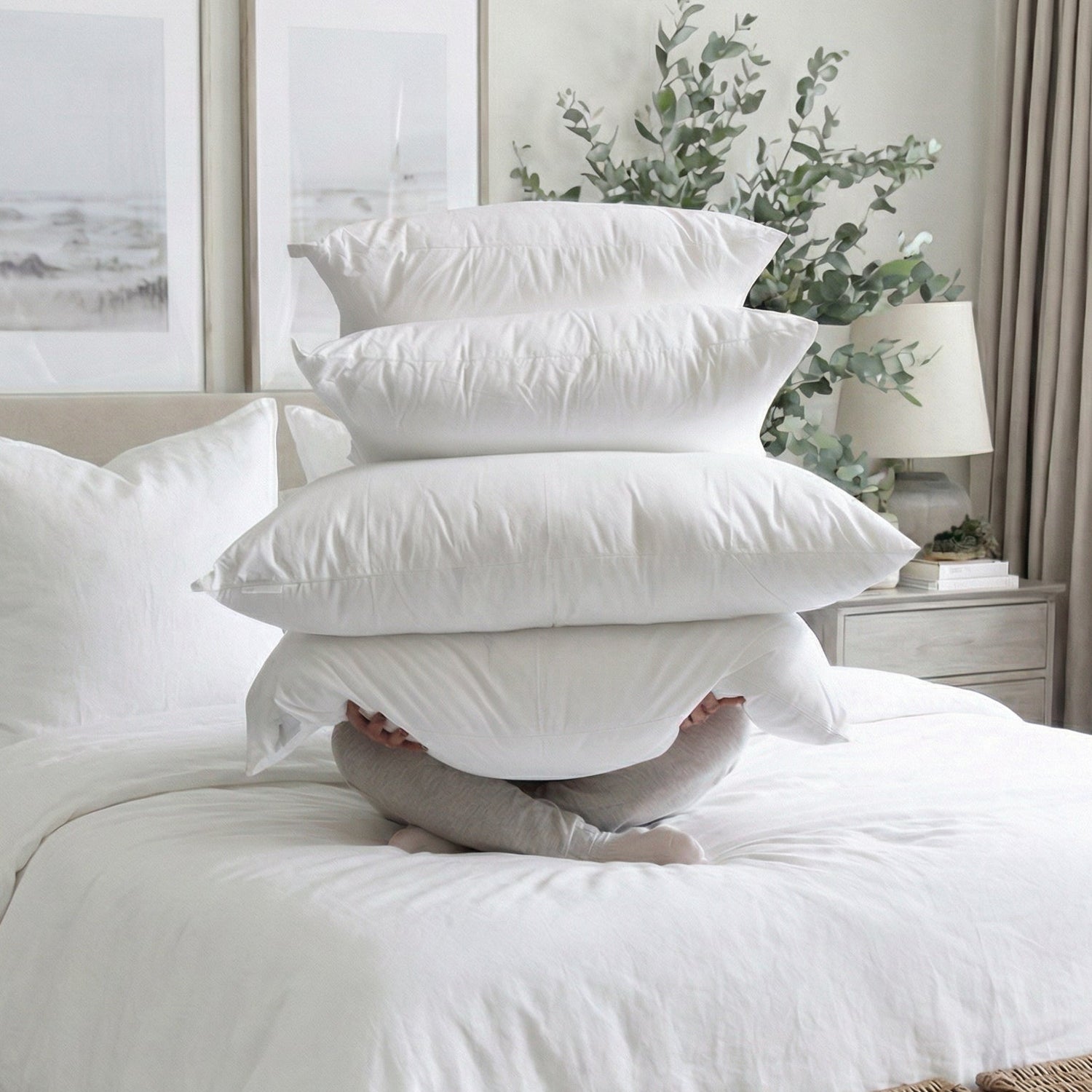 Stack of white pillows on a bed in a bedroom setting with decor elements.
