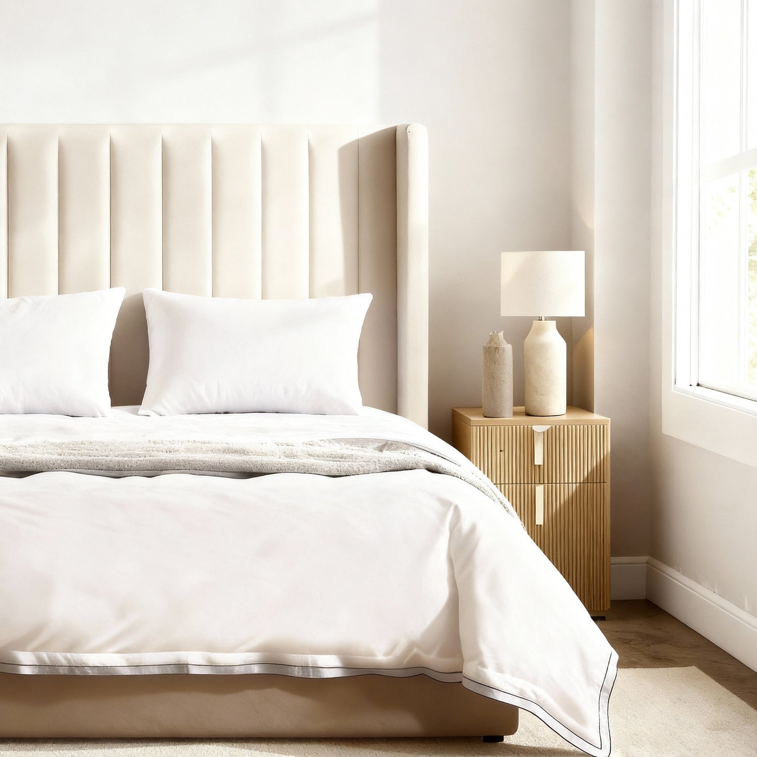 Neatly made bed with white bedding in a bright bedroom.